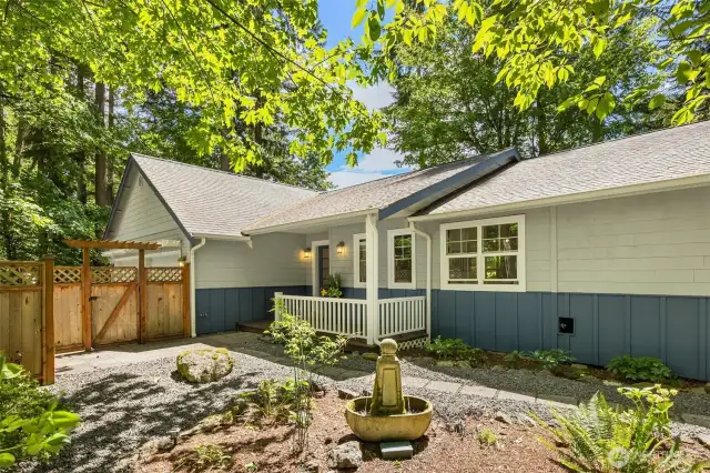 View to the front entry. The gate opens to the paved driveway. The covered front porch is a nice place to sit and take in the garden views.