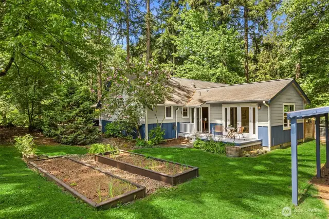 View of part of the backyard with vegetable beds, lawn and a deck with french doors to the primary suite.