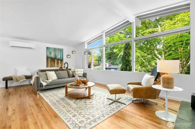 Spacious living room with newly refinished hardwood floors and large west-facing windows that frame the view of the lush surroundings and sunsets. Mid-century details like vaulted ceilings and exposed beams throughout.