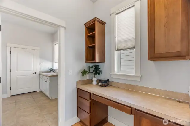 This area is just off the kitchen to the left of the refrigerator. It features a built-in desk area with storage cabinetry  & drawers. To the left, double doors open to a sizable pantry. The laundry room with ceramic tile floors, utility sink & cabinet storage is just beyond and the door ahead opens to the XL 2-car garage.