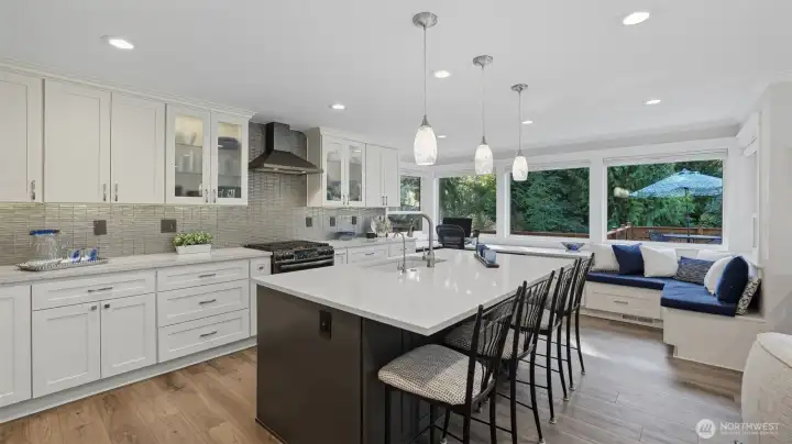 Updated kitchen features a gas cooktop with hooded vent, two ovens with convection feature, designer tile backsplash, glass uppers and pendant lighting