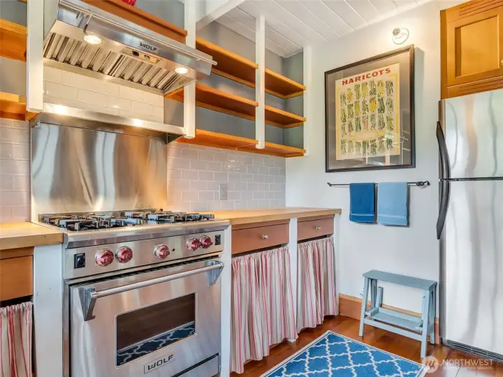 inviting kitchen with a wolf range, stainless steel appliances and custom shelving/cabinetry.