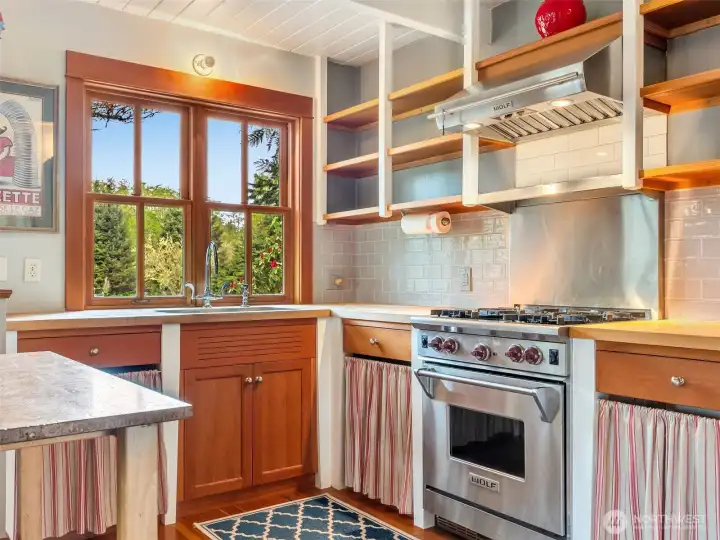 inviting kitchen with a wolf range, stainless steel appliances and custom shelving/cabinetry.