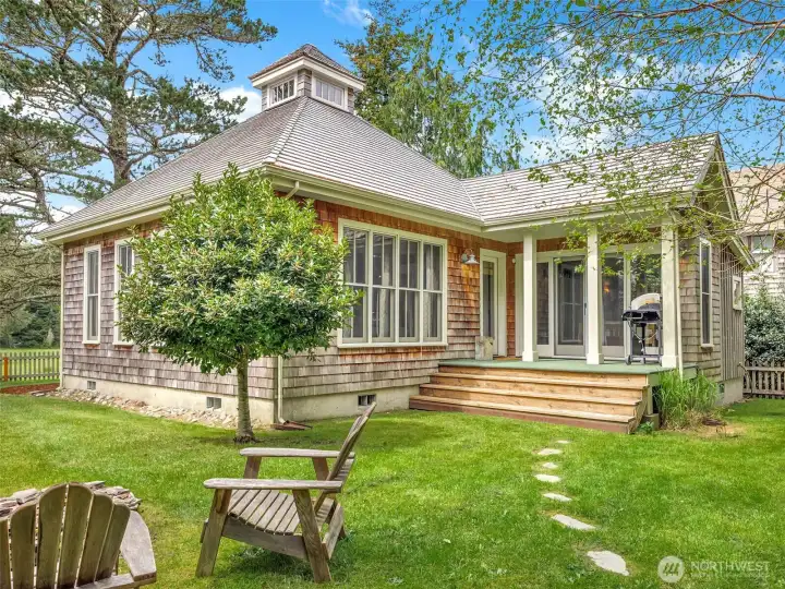 Backyard with lawn and mature landscaping, multiple outbuildings and a fire pit.