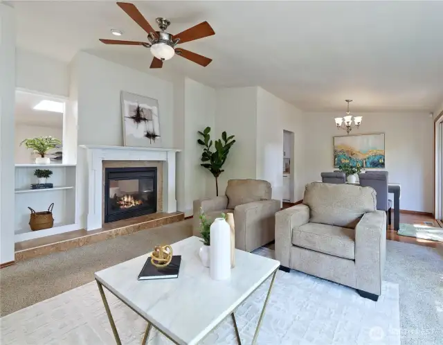 Another view of living room with showing shared fireplace with family room beyond.   Ornate mantle, tile hearth, bookcased, and opening which shares light from skylight in family room