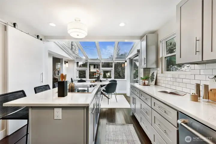 Bright, sun-filled kitchen features an oversized island, quartz countertops, custom cabinetry & generous casual dining space