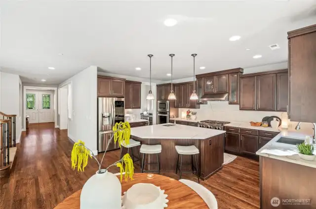 Large center island with veggie sink and beverage fridge, double ovens for effortless hosting, and full-height backsplash that adds texture and style.