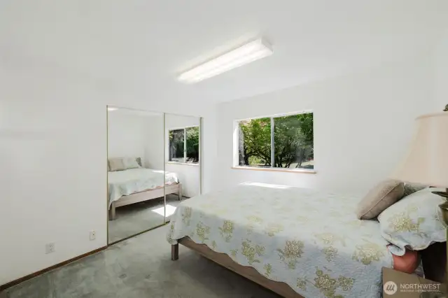 The two additional bedrooms are thoughtfully located at the opposite end of the house from the primary suite, offering privacy and tranquility. In this room, a nice-sized window invites natural light and connects the room to the surrounding beauty, while mirrored double closet doors provide ample storage space as well as enhancing the natural light.