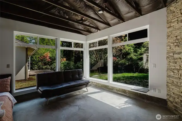 Inside the guest studio with the garage, four large corner windows create a stunning connection to nature—two on each side, meeting at the corner to bring the outdoors in. The effect is immersive, offering the feeling of being nestled in the forest while enjoying the comfort of indoor living. It’s a truly special space that blends light, scenery, and serenity.