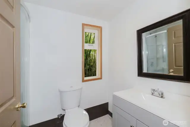 The brand-new bathroom includes a sleek rounded corner shower, new vanity, and toilet—offering fresh, modern convenience in this serene forest retreat.