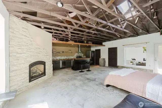 The sleeping area is seamlessly integrated into the open studio layout, with the cozy bed positioned to take full advantage of the natural light and forest views from the corner windows. The thoughtful design, paired with the warm finishes, fireplace, and modern kitchen and bath, creates a self-contained retreat that’s as comfortable as it is inviting.
