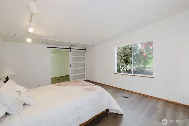 The large primary bedroom boasts beautiful wood laminate flooring and a spacious walk-in closet, highlighted by a stylish barn door with frosted glass panels for added privacy and character.