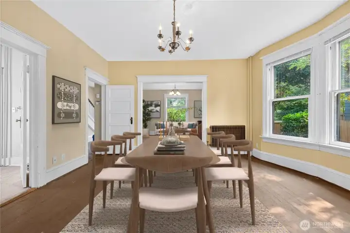 Dining room view toward the spacious living room, with large windows bringing in natural light from the fenced side yard. (Virtually Staged.)