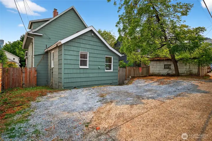 Additional view of the rear parking area, offering convenient off-street access for multiple vehicles. Secured side yard to the left provides bike storage.