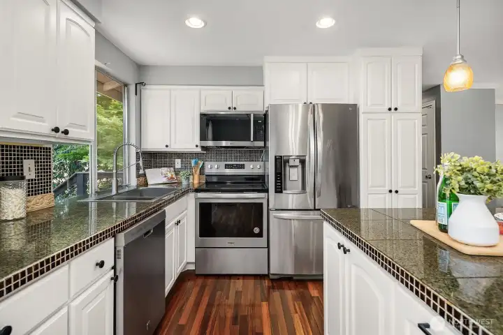 This view showcases the full run of updated white cabinetry, stainless steel appliances, and rich hardwood floors, delivering a polished and highly functional kitchen layout. This view showcases the full run of updated white cabinetry, stainless steel appliances, and rich hardwood floors, delivering a polished and highly functional kitchen layout.