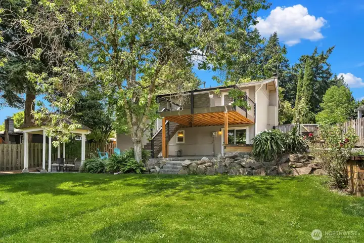 Another backyard view showcases the generous green space, beautiful mature trees, and the entertainer's deck above, highlighting the multiple outdoor living zones this property has to offer. Another backyard view showcases the generous green space, beautiful mature trees, and the entertainer's deck above, highlighting the multiple outdoor living zones this property has to offer.