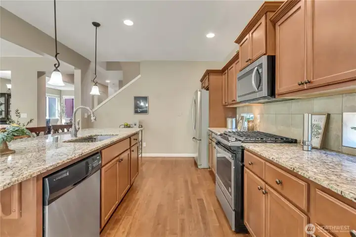 Another View of the Bright, Open Kitchen with Slab Granite Countertops, Tile Backsplash, Wood Cabinets, and Stainless Appliances That Stay.
