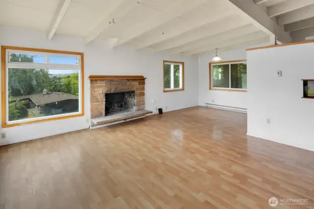 Enter into the living room, with vaulted wood-beamed ceilings and original mid-century stone fireplace. The dining area is in the far corner, and the wall to the right is the open kitchen.