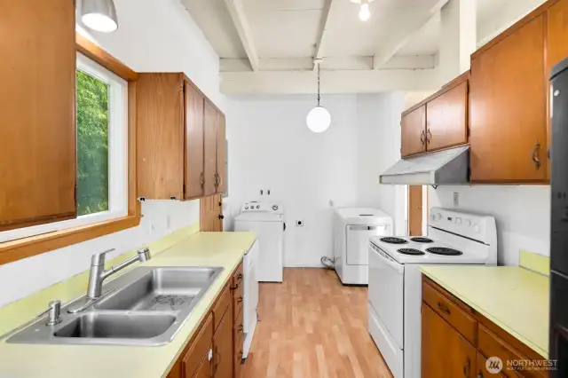 Upstairs kitchen with original wood cabinets and lots of extra space; laundry area in the background, with an exterior door to the backyard on the left side of this photo.