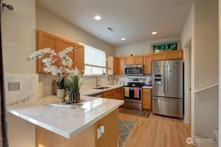 View of kitchen from dining area with stainless appliances and quartz countertops