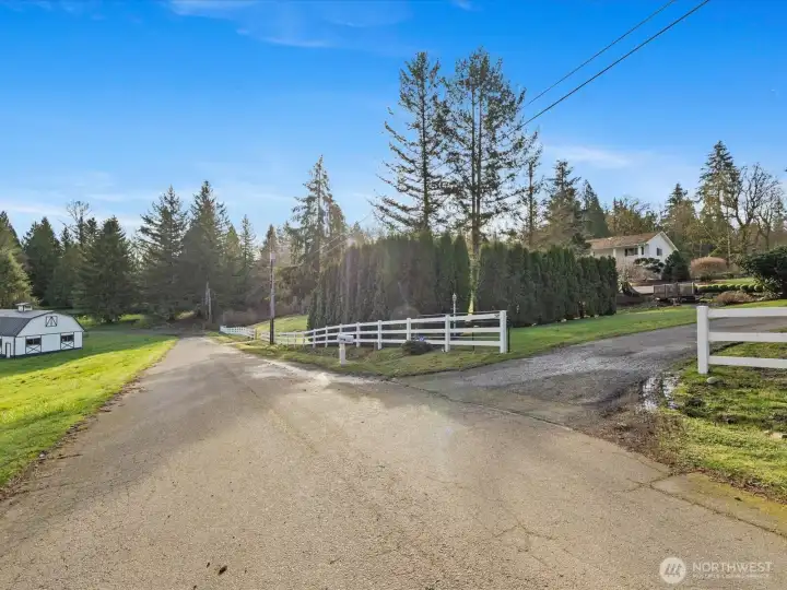 Gated driveway entry with white fencing and long approach, offering privacy and a welcoming first impression.