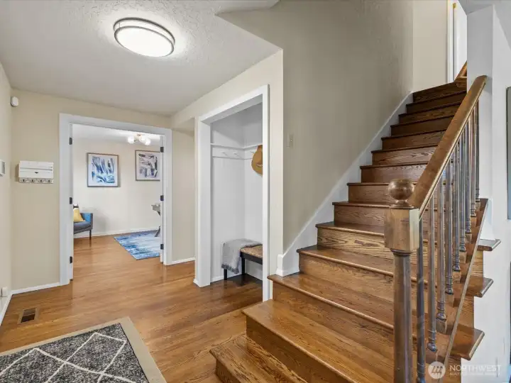 Open stairway with hardwood flooring and nearby coat storage, creating a practical and inviting transition between levels.