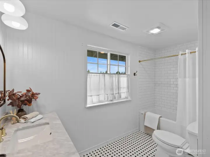 Primary bathroom with tub and tiled shower surround, featuring a window for natural light and a clean, functional layout.