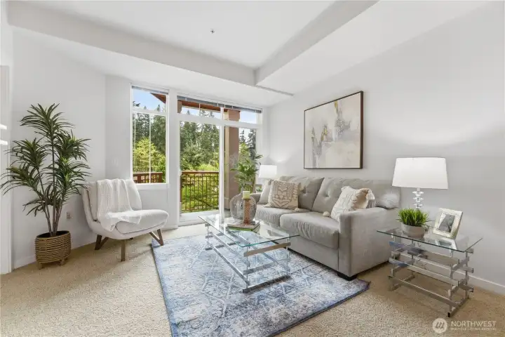Bright living room seating area with large windows and balcony access overlooking lush greenery