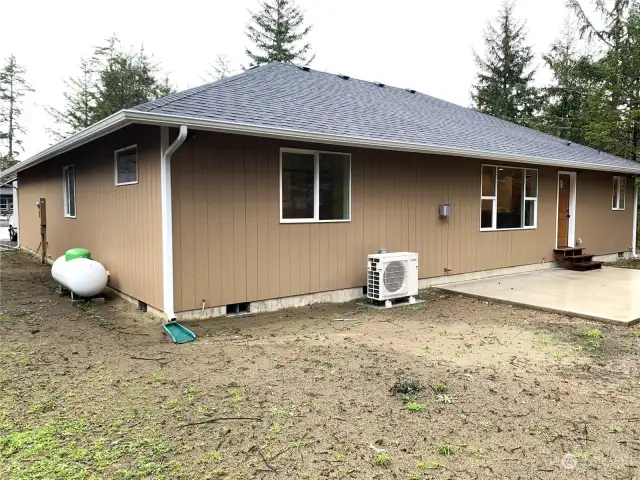 Back corner showing propane tank on the left, ductless heat  pump in the middle and large patio on right