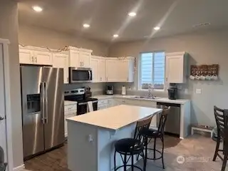Kitchen features Stainless steel appliances, island, & white cabinetry.