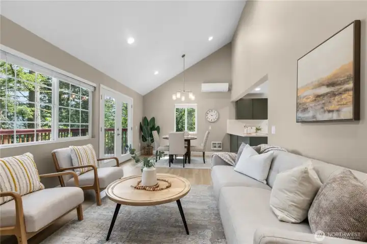 Vaulted ceilings and expansive windows create a light-filled living room centered around a cozy fireplace and peaceful wooded outlooks.
