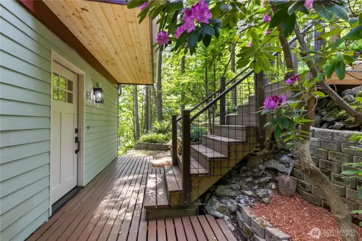 Covered entry deck provides a welcoming transition into the home while surrounded by lush greenery.