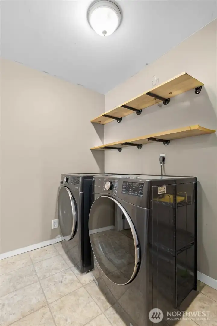 Dedicated laundry room with modern front-loading washer and dryer plus added shelving for storage and organization.