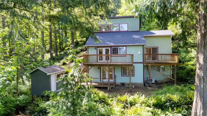 Exterior showcases multiple decks and outdoor gathering spaces surrounded by lush greenery.