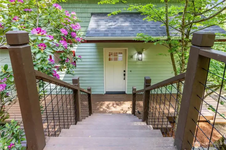 Elevated walkway entry framed by mature landscaping and flowering rhododendrons.