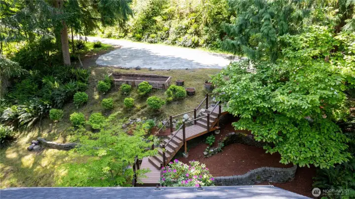 Landscaped upper yard includes an ample parking pad, garden beds, retaining walls, and pathways integrated into the natural setting.
