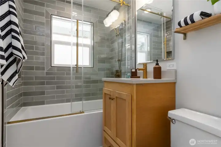 Stylishly updated full bathroom featuring a tiled shower-tub combo with glass doors and modern finishes.