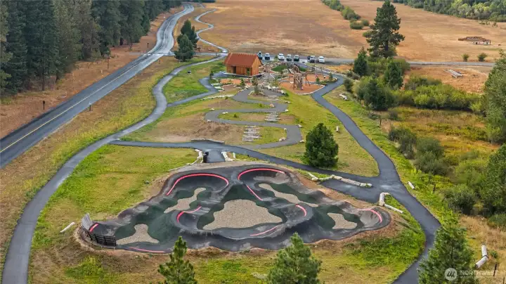 Nelson Farm Playground offers modern climbing structures, slides and swings, a balance of agility elements, open grassy areas for free play, picnic tables, and shaded seating nearby.