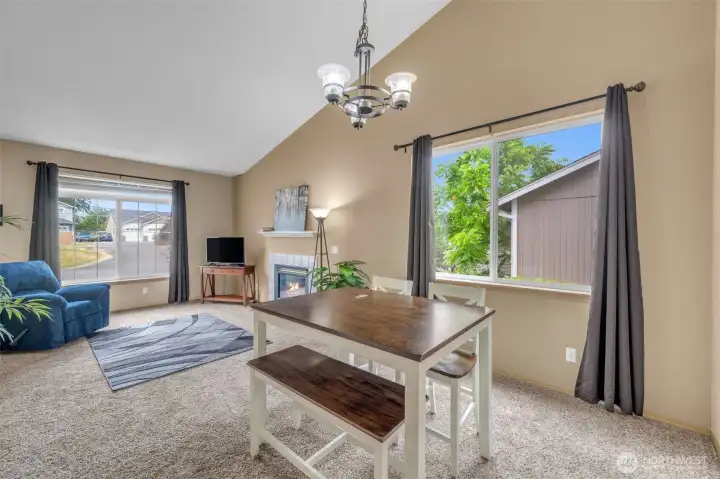Open-concept dining and living areas offer an inviting layout with vaulted ceilings, abundant natural light, and a cozy gas fireplace, creating the perfect gathering space.