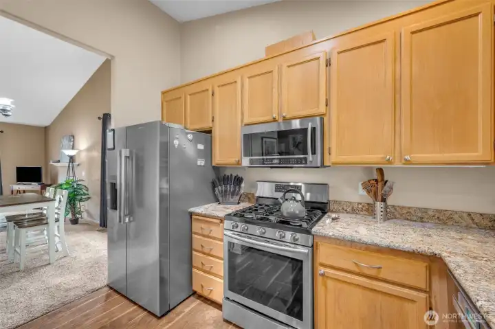 Bright kitchen with granite countertops, stainless steel appliances, ample maple cabinetry, and a large window overlooking the backyard that brings in plenty of natural light.