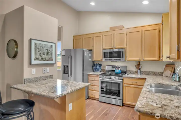 Functional kitchen with warm maple cabinets, granite countertops, stainless steel appliances, gas range, and convenient breakfast bar seating—perfect for casual dining and entertaining.