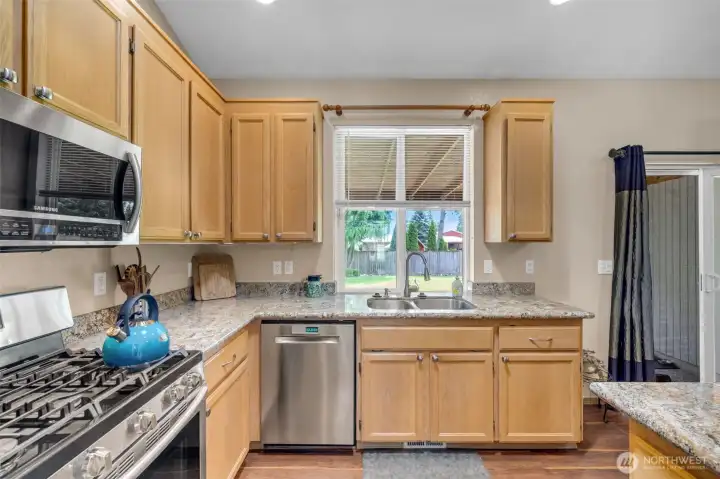 Thoughtfully designed kitchen with abundant maple cabinetry, expansive granite countertops, stainless steel appliances, and a large window overlooking the backyard for plenty of natural light.
