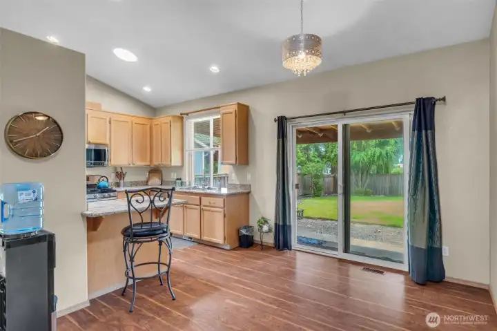 Bright kitchen and dining nook featuring granite countertops, maple cabinetry, stainless steel appliances, recessed lighting, and a sliding glass door leading to the covered patio and fully fenced backyard.