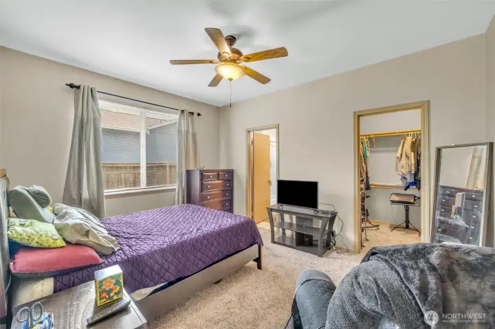Spacious primary suite featuring plush carpeting, ceiling fan, large picture window, and a walk-in closet, creating a relaxing private retreat.