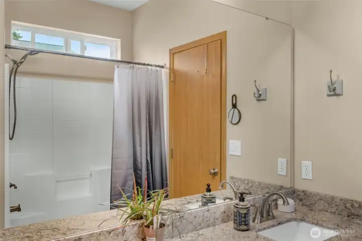 Primary en-suite features a dual-sink granite vanity, oversized mirror, linen closet, and a tub/shower combination with a transom window that provides natural light while maintaining privacy.