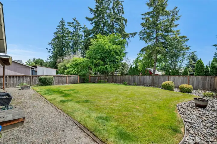 Beautiful park-like setting with privacy fencing, mature evergreens, and low-maintenance rock borders surrounding the spacious backyard.