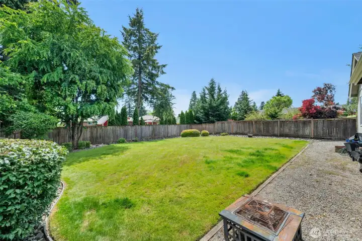 Expansive, fully fenced backyard with a lush level lawn, mature shade trees, and established landscaping—offering plenty of space for play, pets, gardening, or entertaining.