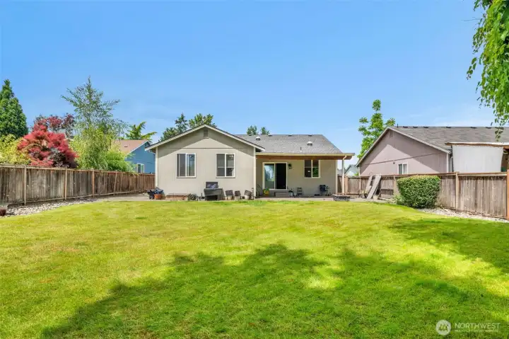 Large, fully fenced backyard with an expansive lawn and covered patio—ideal for entertaining, gardening, or simply relaxing outdoors.