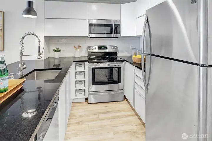 Open kitchen with black quartz countertops and modern updated white cabinets.