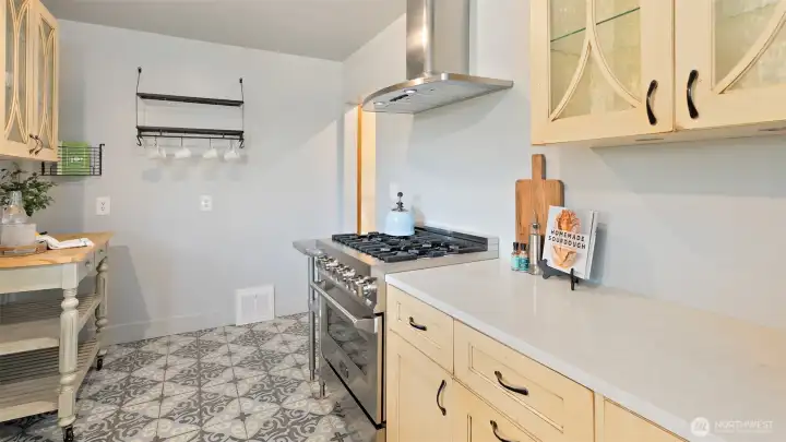 Just look at that gorgeous floor tile! This side of the kitchen features more glass-front cabinetry, a smooth quartz countertop, and a professional-style six-burner gas cooktop with a sleek hood overhead - combining everyday function with standout design.